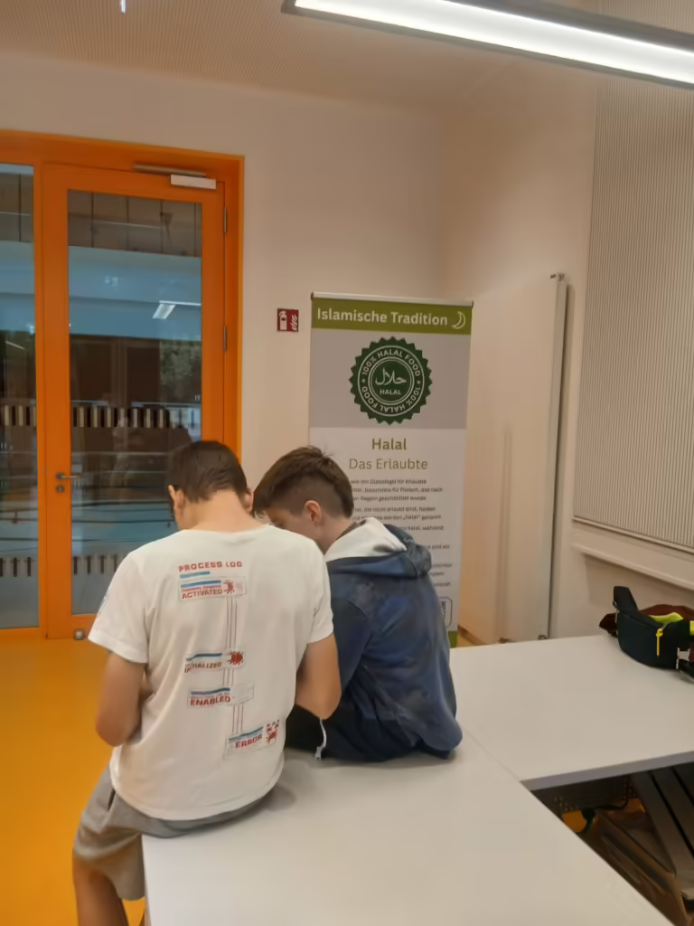 Zwei Schüler an einem Tisch vor einem Banner der islamischen Tradition