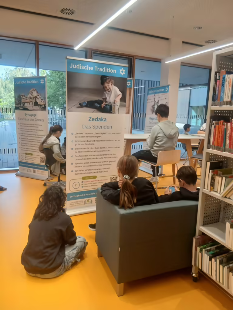 Jugendliche sitzen in der Schulbibliothek vor einem Banner der jüdischen Tradition