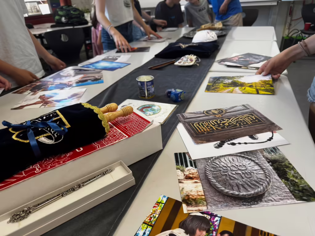 Bildimpulse und religiöse Gegenstände auf einem Tisch, darunter eine kleine Torarolle und ein Teller mit arabischer Kalligrafie
