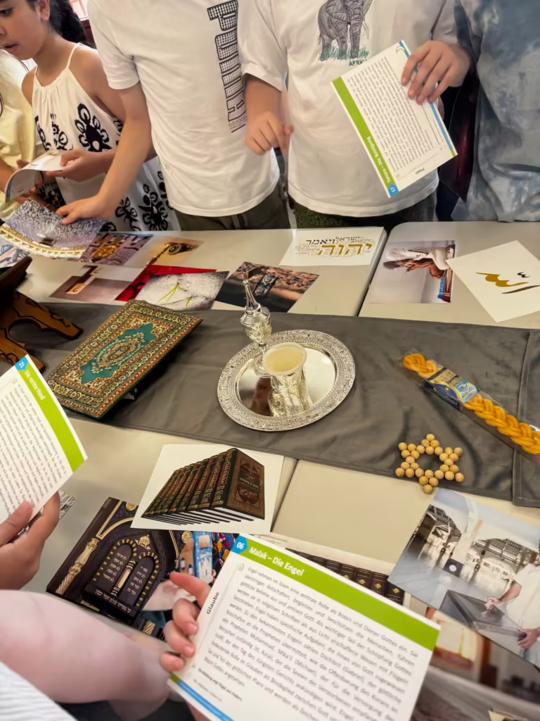 Schülerinnen und Schüler lesen Lernkarten an einem Tisch mit Gebetsteppich, Gebetskette und Becher